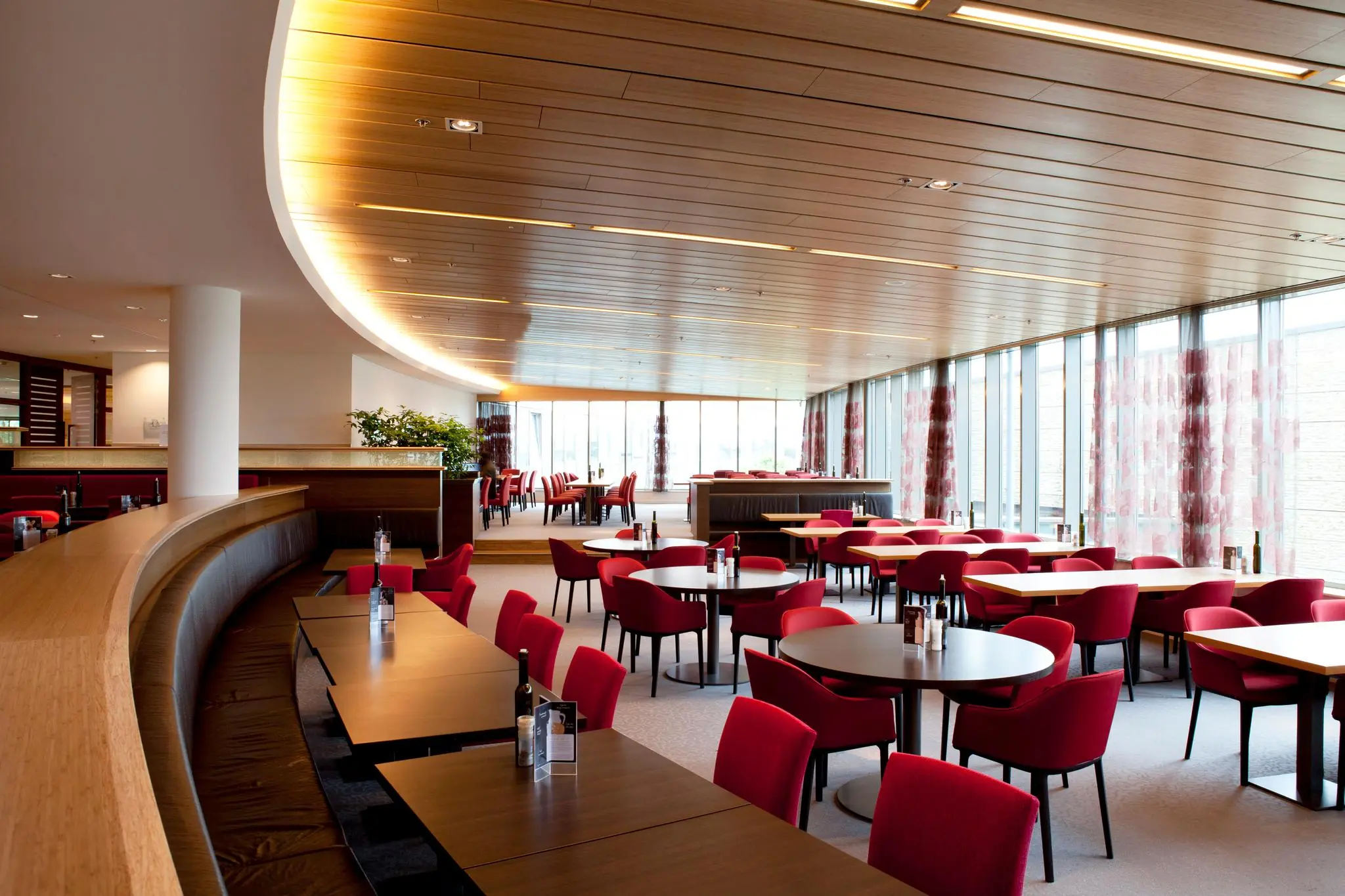 Moderne en ruime bedrijfskantine aan de Laan van Langerhuize met rood meubilair en grote ramen.